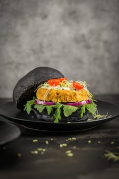 Tasty grilled veggie burgers with chickpeas and vegetables on black bread on dark wooden countertop.