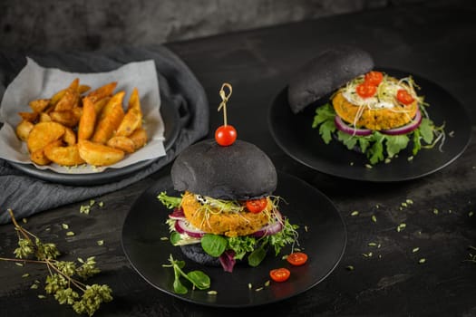 Tasty grilled veggie burgers with chickpeas and vegetables on black bread on dark wooden countertop.
