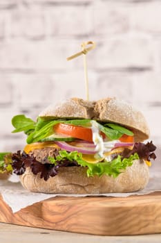 Healthy vegan burger with fresh vegetables and yogurt sauce on rustic kitchen counter top.