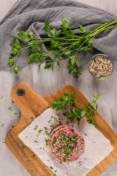 Raw veggie burger with beetroot and white beans with parsley leaves on wood cutting board.