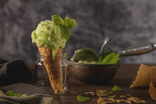 Pistachio ice cream in a dark rustic bowl and waffle cone on a brown wooden background.