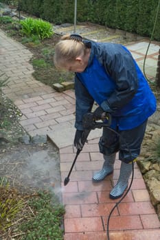 Woman cleans stone slabs with a pressure washer