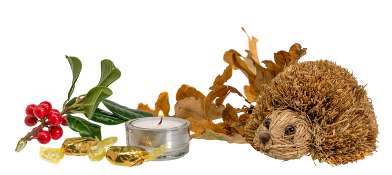 Christmas decoration with autumn leaves, candle and straw hedgehog in front of white background