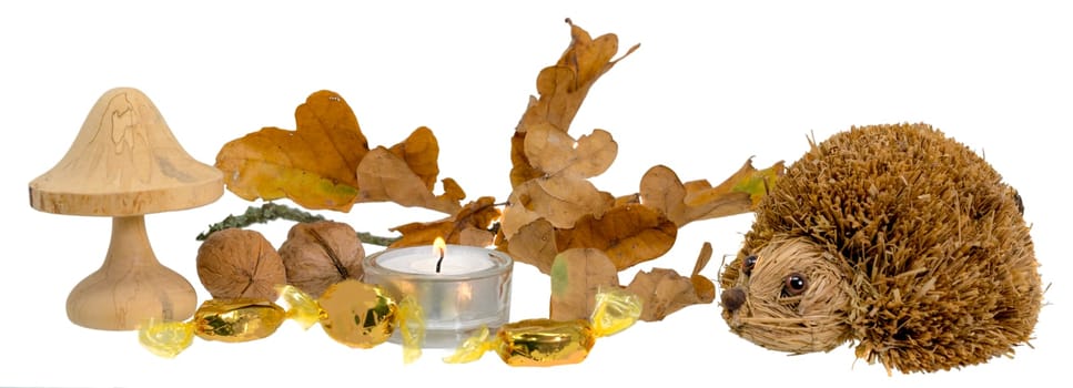 Christmas decoration with autumn leaves, candle, wooden mushroom and straw hedgehog in front of white background