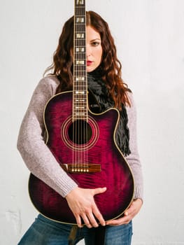 Young beautiful redhead woman holding an acoustic guitar over her face.