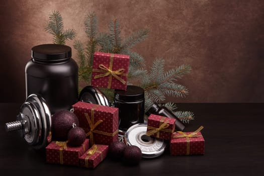 Sports nutrition (supplements), sports equipment, fir branch and gift boxes on dark brown background with copy space. Fitness, sport, healthy lifestyle concept. New Year. Christmas.