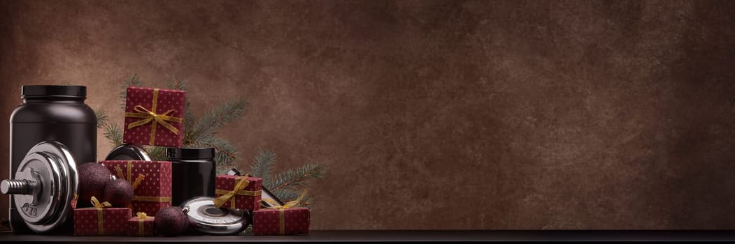 Sports nutrition, sports equipment, fir branch, gifts, Christmas ornaments on dark brown background with copy space. Fitness, sport, healthy lifestyle concept. New Year. Christmas. Banner background