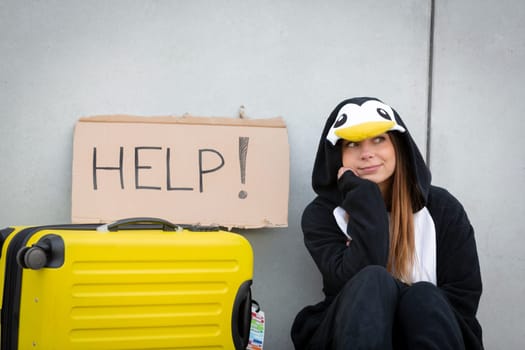 Young woman, with penguin costume and yellow suitcase, has to travel due to global warming. Symbolizes a sad penguin who has to leave his homeland because of global warming or climate change.