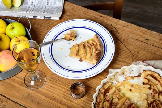 apple pie on a table with apples and glass of cider