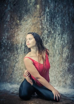 Woman practicing yoga near waterfall. Twisted lotusl Pose. Bharadvajasana