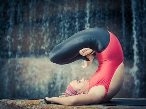 Woman practicing yoga near waterfall. Pose with legs in Padmasana