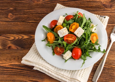 light salad of arugula, tomatoes and feta cheese on a wooden background