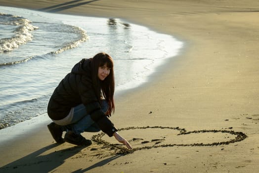 A portrait of a nice girl writing and drawing on sand to the seaside in winter