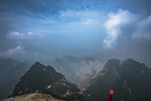 Raised in the air tourist hand in a desperate like falling gesture with the panoramic view from the West Peak summit of the inspiring, sacred and majestic Huashan mountain, famous tourist attraction, Shaanxi province, China