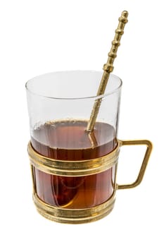 Glass with metal handle and spoon of bronze filled with hot tea isolated on white