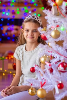 Beautiful girl sits by a white Christmas tree