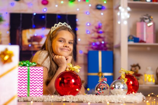 Beautiful ten-year-old girl lies on a rug in the New Year’s interior and looks at the frame cheerfully