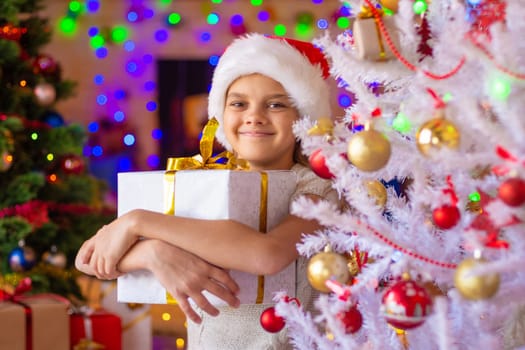The girl at the Christmas tree holds a big gift in her hands