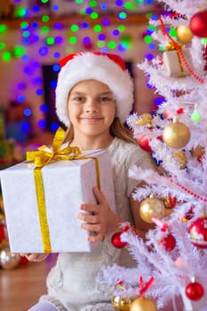 Girl sitting by the Christmas tree with big gifts in her hands