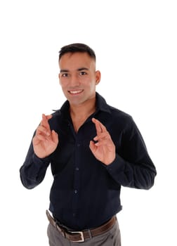 A young East Indian man standing in a black shirt in the studio, crossing.his fingers to have luck, isolated over white background.