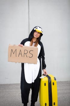 Young woman, with penguin costume and yellow suitcase, has to travel due to global warming. Symbolizes a sad penguin who has to leave his homeland because of global warming or climate change.