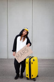 Young woman, with penguin costume and yellow suitcase, has to travel due to global warming. Symbolizes a sad penguin who has to leave his homeland because of global warming or climate change.