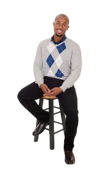 A young handsome African American man sitting full body in the.studio, thinking and smiling, isolated for white background.