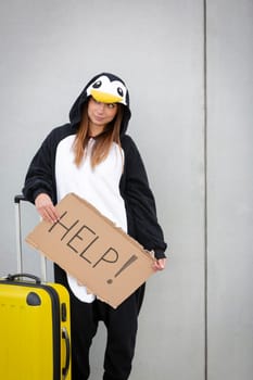 Young woman, with penguin costume and yellow suitcase, has to travel due to global warming. Symbolizes a sad penguin who has to leave his homeland because of global warming or climate change.