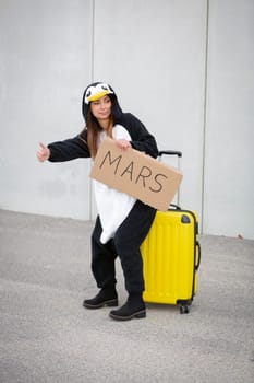 Young woman, with penguin costume and yellow suitcase, has to travel due to global warming. Symbolizes a sad penguin who has to leave his homeland because of global warming or climate change.