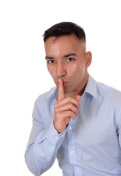 A close up image of a young East Indian man in a blue shirt with his .finger over his mouths, don't talk, isolated for white background.