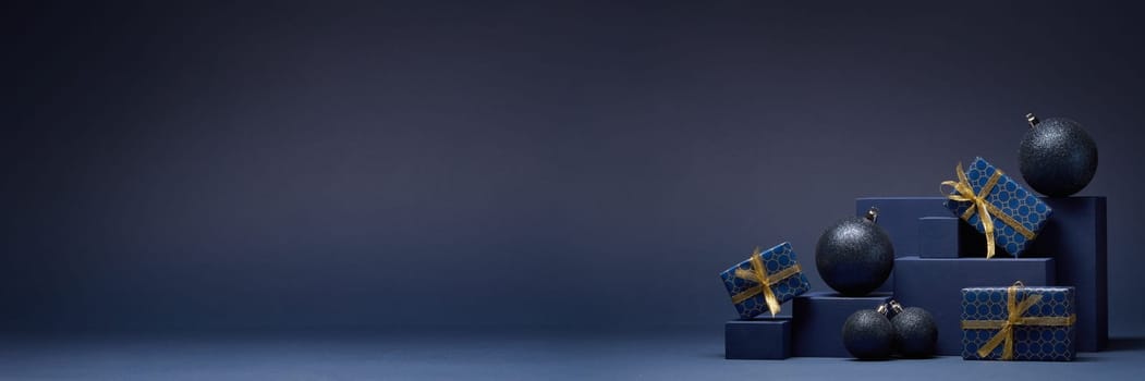 Composition with blue geometric figures, gift boxes and Christmas ornaments on dark blue background with copy space. Christmas. New Year. Shopping. Sale. For design of advertising, greeting card