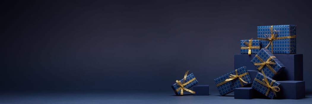Composition with blue geometric figures and gift boxes with golden ribbon on dark blue background with copy space. Christmas. New Year. Shopping, sale concept. For design of advertising, greeting card