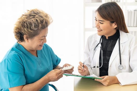 Asian female doctor talking prescribing pills to old senior elderly patient in examination room of clinic hospital.