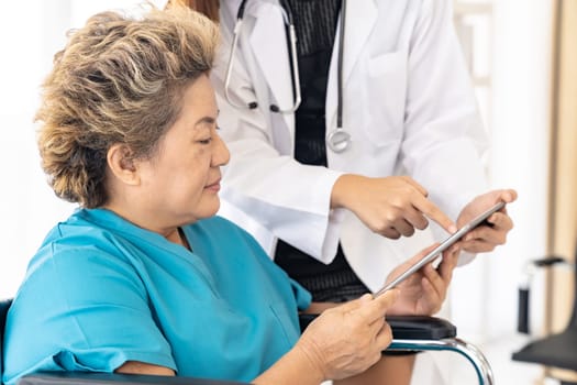 Asian confidence doctor using digital tablet expressing health concerns with old elderly woman patient sit on wheelchair