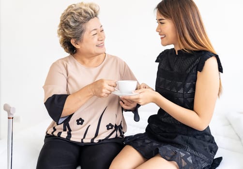 Caregiver woman giving coffee to old elderly woman on the bed and check up her at home.