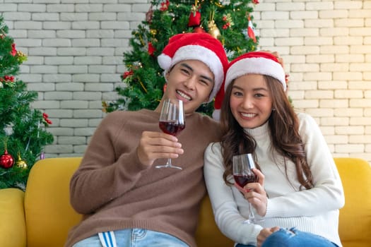 Young asian adult teenager couple celebrateing christmas holiday with wine together in living room with christmas tree decoration.