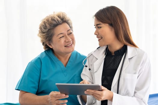 Asian confidence doctor using digital tablet expressing health concerns with old elderly woman patient sit on wheelchair