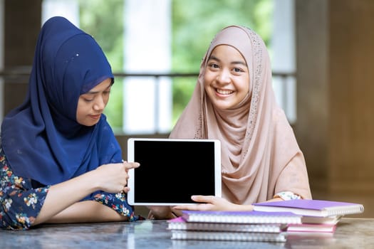 Teenager Young Adult Asian Thai Muslim university college students holding digital tablet and pile of books using for education and online education concept