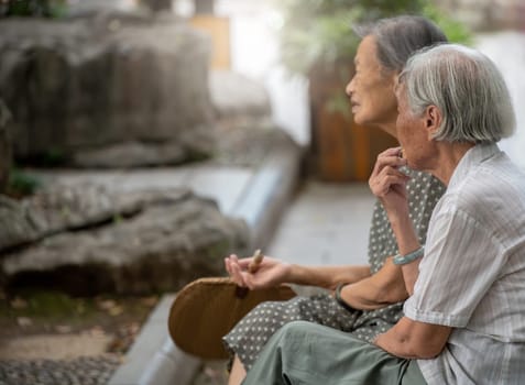 Guilin, China -  August 2019 : Portrait of two old retired chinese asian women sitting on a bench by the Shan Lake in a park  in summer