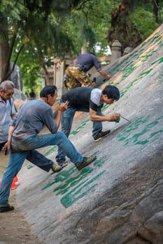 Huashan, China -  August 2019 : Man painting chinese calligraphy characters on a large boulder in the courtyard of a Buddhist temple at the foot of Huashan mountain, Xian, Shaanxi Province