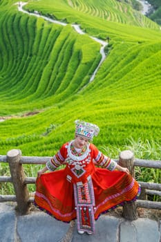 Pingan, China -  August 2019 : Chinese woman dressed in traditional decorated red folk costume posing for photos on a Nine Dragons and Five tigers viewpoint, Longji Rice Terraces, Pingan village, northern Guilin, Guangxi Zhuang Autonomous Region, Guangxi Province
