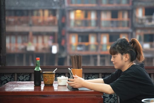 Feng Huang, China -  August 2019 : Chinese woman sitting in a cafe restaurant and using her tablet to watch clips or work, Fenghuang Old Town