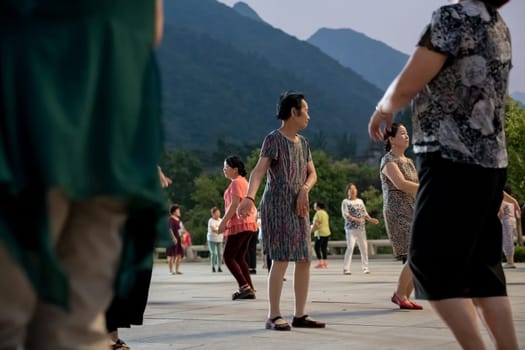 Huashan, China -  August 2019 : Group of Chinese women dancing in the open plaza square at the foot of HuaShan mountain at dusk, Shaanxi Province