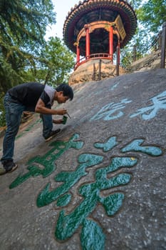 Huashan, China -  August 2019 : Man painting chinese calligraphy characters on a large boulder in the courtyard of a Buddhist temple at the foot of Huashan mountain, Xian, Shaanxi Province