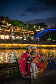 Feng Huang, China -  August 2019 : Chinese family female generations dressed in traditional folk costumes posing for a photo on the riverbank of Tuo river, flowing through the centre of Fenghuang Old Town