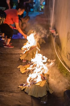 Feng Huang, China -  August 2019 : People burning paper on streets and pavements in a religious festival ceremony to pay respect to ancestors and spirits