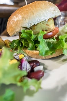 Healthy vegan burger with tomato, baked potatoes, beans, onions, salad. Close-up.