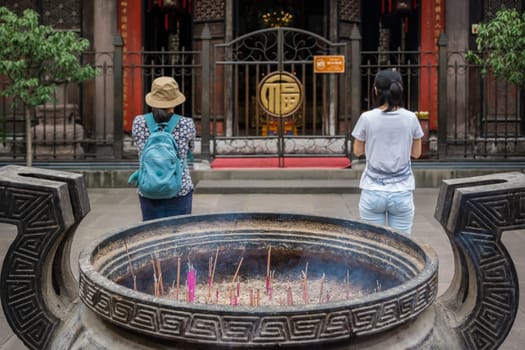 Chengdu, China -  July 2019 : Chinese woman and man praying, worshiping, burning incense sticks, giving alms and thanks at the Wenshu Chinese Buddhist Temple