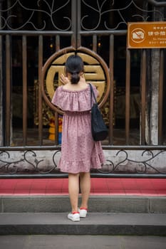 Chengdu, China -  July 2019 :  Chinese woman lightening a fire to an incense stick at the gates to the temple in Wenshu Monastery