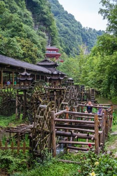 Wulingyuan, China - August 2019 : Man and child using legs to pull levers on a wheel of an old Water wheel in Huanglong Yellow Dragon Cave scenic area, Zhangjiajie, Hunan Province